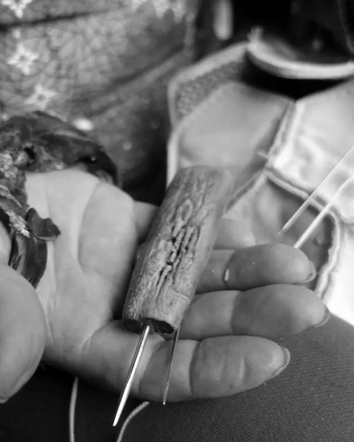 A ballmaker&rsquo;s hand holding the awl and waxed thread beside a half-stitched ball.