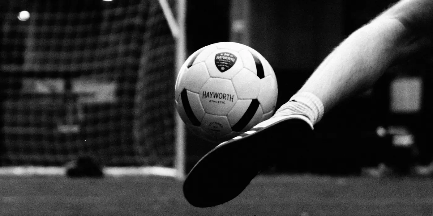A boot swinging through a Hayworth ball in front of the goal, under an overpass, in black and white. Photograph by Javid Gomez.